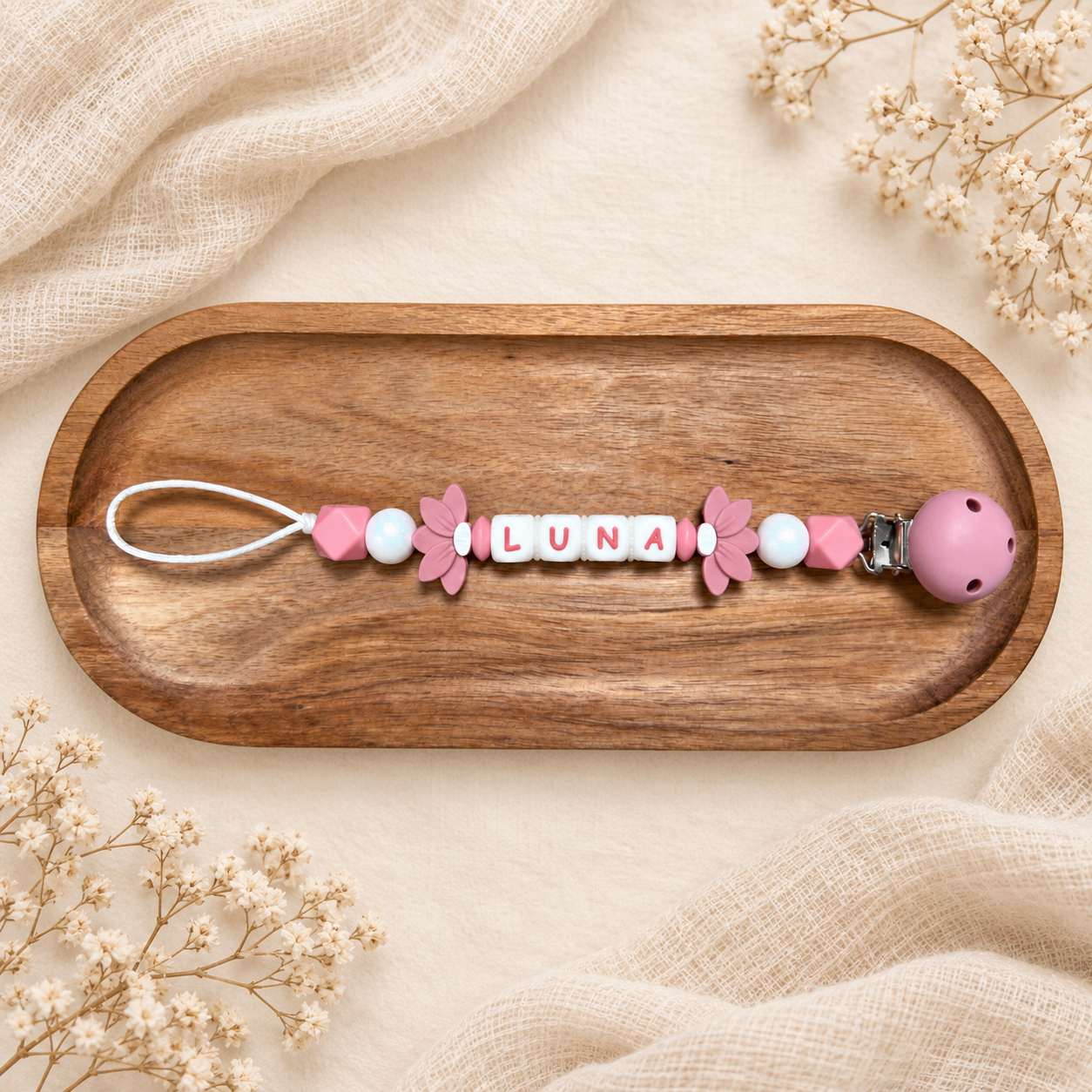 Attache-tétine personnalisée avec fleurs roses, présentée sur un plateau en bois